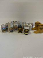 Full view of all eight ceramic salt and pepper shakers arranged in two rows, showing various souvenir designs and shapes including boots and cylindrical jars.