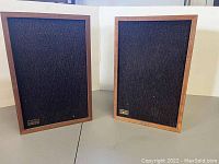 Pair of vintage teak wood speakers with black fabric grills on a grey surface.
