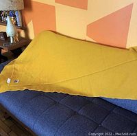 Mustard yellow wool blanket folded and laid over a blue cushioned surface, showing label and edge stitching.