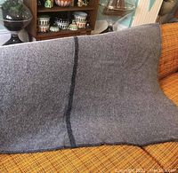 Photo of the gray wool blanket with a dark vertical stripe near one edge, spread over an orange patterned couch.