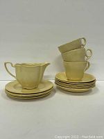 Photo of yellow Petal Ware creamer, four stacked teacups, and six side plates arranged in a pile.