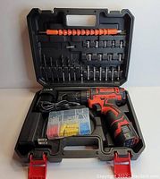 Open black plastic carrying case containing Aotui cordless drill, battery charger, multiple drill bits and screwdriver bits, socket heads, flexible drill extension, and plastic box of wall anchors.
