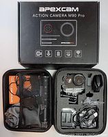 Photo of the Apexcam M90 Pro action camera box and the open travel case with camera and accessories such as charger cables, mounts, battery, and remote shown inside.