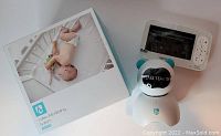 White and blue Heimvision HM136 baby video monitoring system components including PTZ camera, 5-inch LCD monitor with control buttons, and original box showing baby image in crib