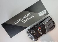 Photo showing the original black and silver Intelligent Heating product box with one pair of black and gray heated gloves still in a sealed plastic bag.