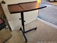 Full view of adjustable height bed side table with wooden top and metal base on caster wheels.