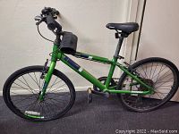 Side view of the green Diamondback boys mountain bike against a wall showing front and rear wheels, handlebars, seat, and pedals