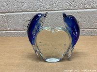 Photo showing front view of two blue glass dolphins attached to a clear heart-shaped glass base with bubbles inside