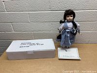 Full display photo showing the Dorothy doll standing on a metal stand, with the original box and certificate laid out beside her.