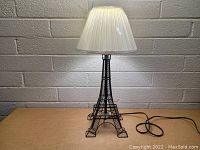 Full frontal view of the Eiffel Tower lamp turned on, showing the lamp shape and the pleated white lampshade.