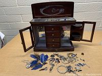 Jewelry box open with assorted jewelry displayed outside on table.