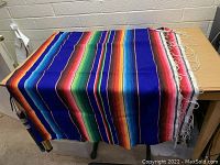 Full view of the large colorful throw blanket folded and displayed, showing vibrant stripes and fringed edges.