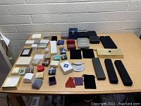 Photo showing a large assortment of jewelry boxes and pouches spread out on a wooden table against a brick wall background.