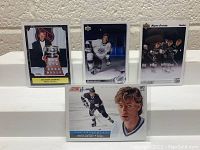 Four Wayne Gretzky hockey cards arranged in two rows, each card in a protective sleeve, showing different poses and trophies.