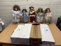 Five porcelain dolls standing on a table behind three boxes, showing front view.