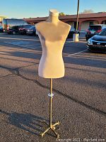 Front view of the beige fabric-covered female torso mannequin dress form on an adjustable metal stand with tripod base.