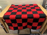 Black and red square checkerboard patterned knitted blanket spread on a wooden table.