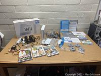 Lot contents arranged on table showing Nintendo Wii console, original box, controllers, games, cables, sensor bar, manuals, and other accessories.