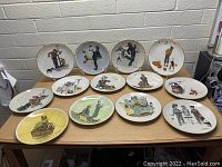 Set of 14 large Norman Rockwell collector plates with different illustrated scenes displayed on wooden tables in a basement or storage area.