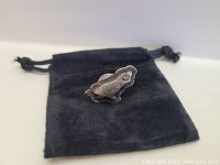 Sterling silver quail pin resting on a black drawstring pouch, showing texture and shape of the pin.