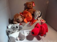 Photo showing all six original Beanie Babies with tags: brown teddy bear, beige lion, orange goldfish, grey and black anteater, grey and white koala, and red dog.