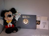 Full lot image showing plush Mickey Mouse doll, MGM Studios commemorative medallion in folder, and medallion pins in case.