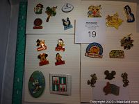 Top down photo showing 19 Disney pins arranged on a lined notebook with a ruler beside them.