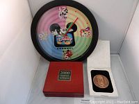 Photo displaying Radio Disney wall clock with black frame and colorful Disney character dial alongside red presentation box holding Walt Disney gold medallion.