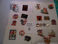 Full view of 20 Disney enamel pins displayed on lined paper, showing various styles and themes including characters and event commemorations.