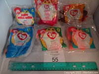 Top view of six unopened McDonald's Ty Beanie Babies sealed in original plastic bags featuring Ronald McDonald hands holding Ty heart logo, numbered and labeled with character names.