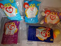 Photo showing five unopened Ty Beanie Babies from McDonald's in original sealed packaging bags with visible numbers and branding.