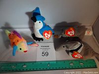 Four original TY Beanie Babies mini plush toys with identifiable tags: a rainbow fish, a blue and white bird, a gray dolphin-like marine animal, and another gray marine animal with orange fins, displayed with a ruler for scale.