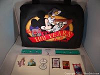 Front of black Disney 100 Years of Dreams pin book with six enamel pins laid out in front.