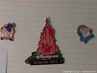 Close-up of three Disney-themed enamel pins including pink Disneyland Paris castle commemorative pin and character pins Dopey and Doc.