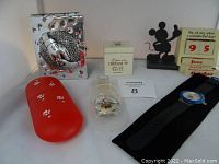 Full view of lot items including the aluminum picture frame, porcelain trinket box, perpetual calendar, a red silicone case, and two watches in packaging.