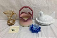 Group photo of all four items: pink satin basket, gold and white spatter pitcher, white nesting hen dish, blue trinket dish.