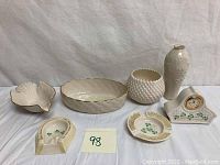 Overall lot showing two ashtrays, a clock, two vases, and two serving dishes arranged on white cloth.