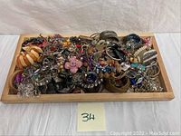 Wide view of the jewelry assortment in a wooden tray showing various bracelets, necklaces, and pins
