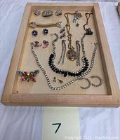 Wooden tray holding assorted costume jewelry including necklaces, bracelets, brooches, earrings, and pendants spread neatly.