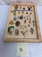 Full overview of costume jewelry displayed on a wooden tray showing varied brooches, rings, earrings, and a bracelet.