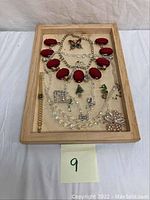 Wooden tray holding costume jewelry including multiple necklaces, brooches, pins, and wrist timer.