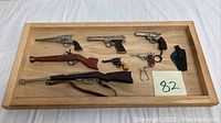 Full lot of seven miniature toy firearms placed on a wooden tray (tray not included in sale).