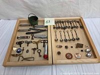 Full overview of two wooden trays holding assorted souvenir spoons, pins, can openers, clock keys, and small collectibles.