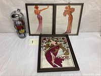 Full lot view showing three framed prints (Laroche and two pin-up girls) and the cocktail shaker with Parisian theme.