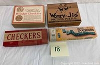 Four boxed vintage games laid out including Williamsburg Wooden Checkers, Woozy-Jig Picture Puzzle, Dragon Dominoes, and Holmes Checkers.