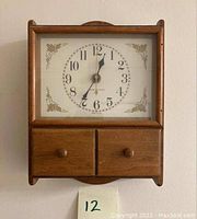 Front view of the vintage General Electric clock showing wooden frame, clock face, and two small drawers below.