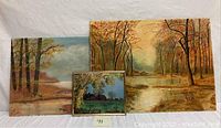 Three paintings arranged with smallest in front showing a barn scene and two larger paintings behind showing autumn forest and water landscapes