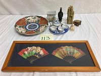 Full lot laid out on a white surface showing plate, vase, tea set, figurines and framed fans.