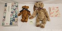 Photo showing the large beige curly fur teddy bear with scarf and the smaller brown teddy bear with ribbon, alongside original packaging box.