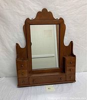 Front view of vintage wooden wall mirror with multiple drawers and decorative scalloped top crest.